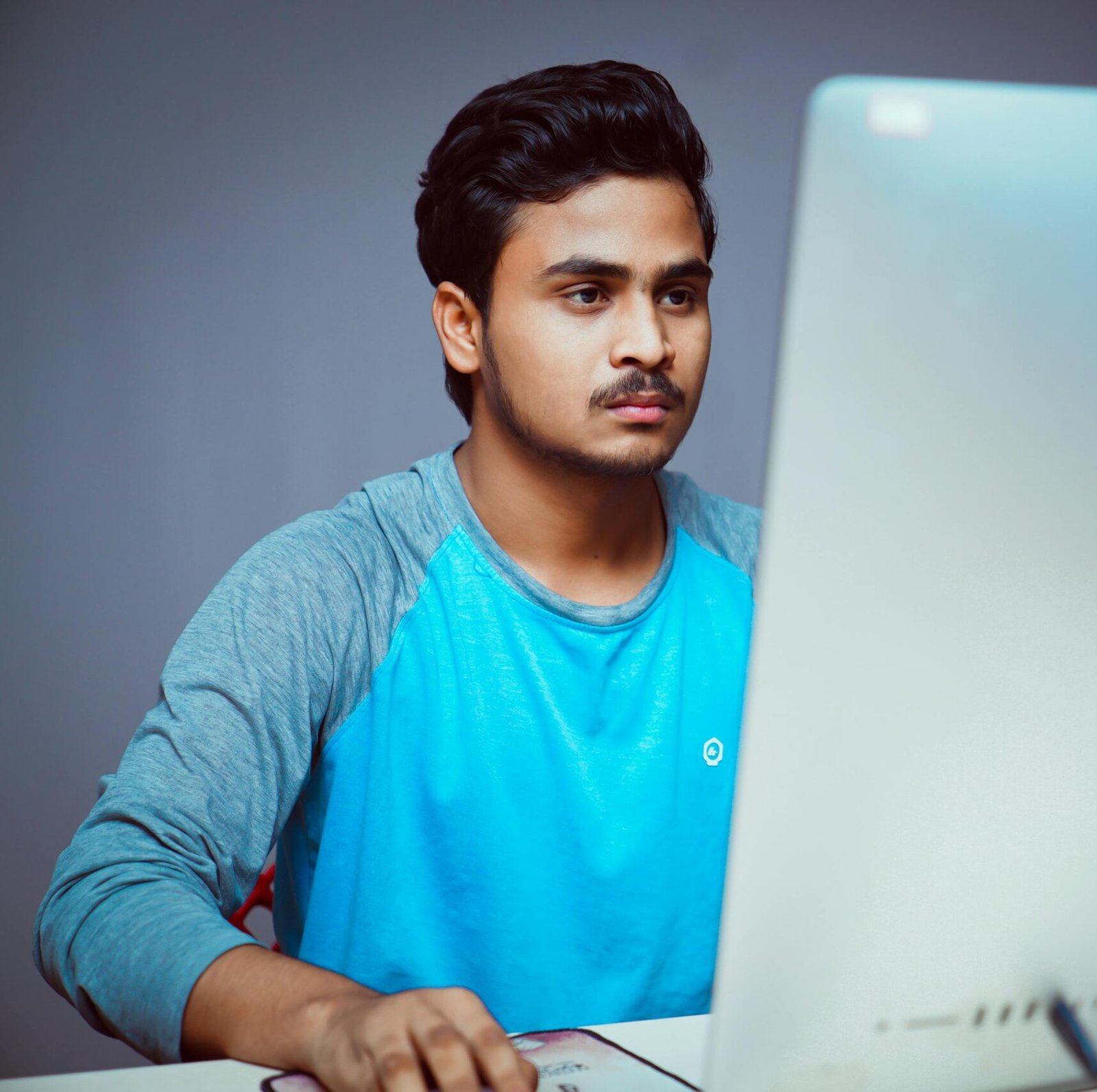 A young man concentrating while working on a desktop computer at home, emphasizing remote work and concentration.